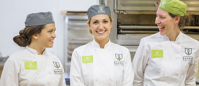 Three Natural Chef students at Bauman college smiling & laughing in the kitchen